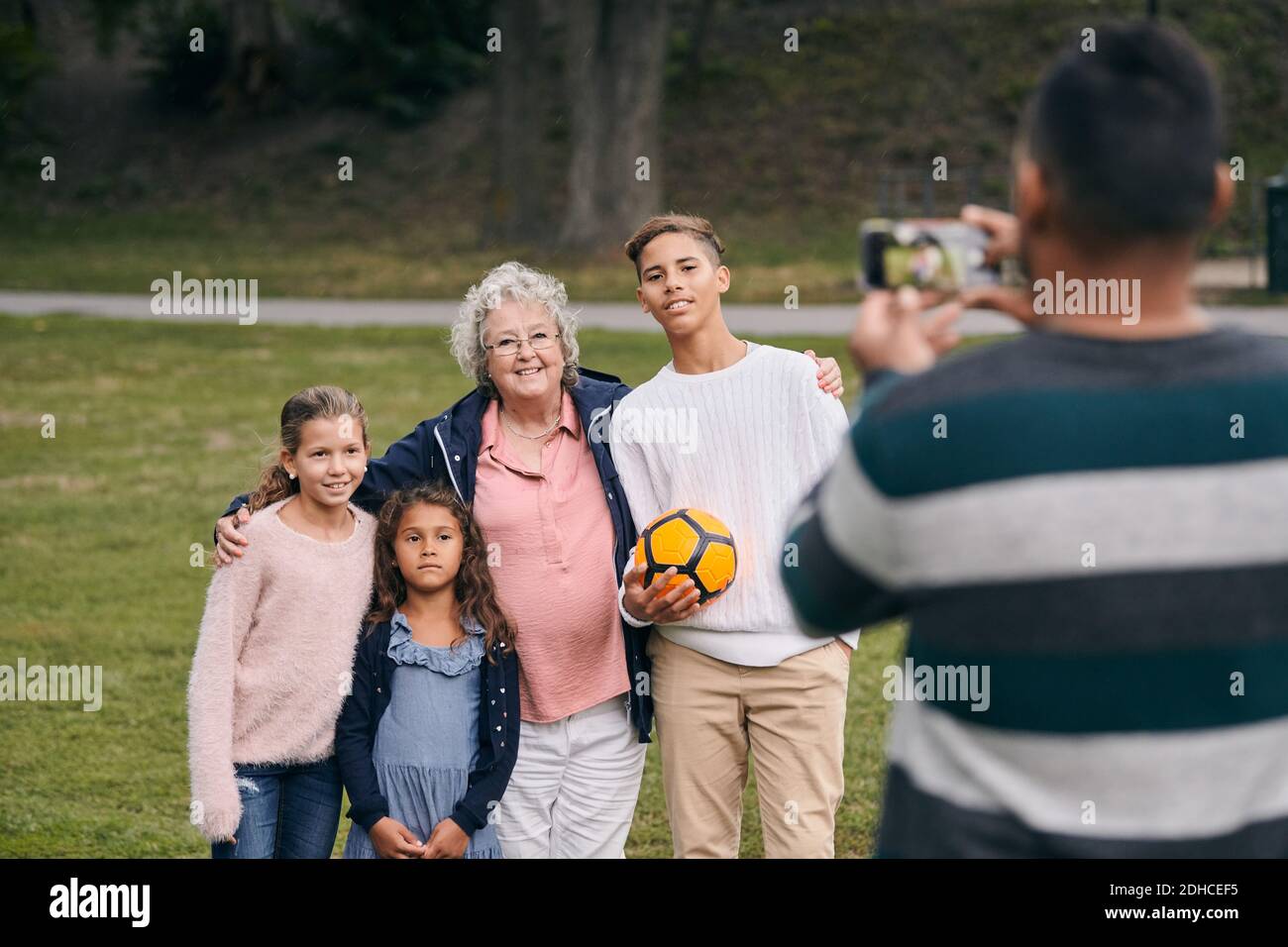 Rückansicht des Mannes, der glückliche Großmutter und Enkelkinder in fotografiert parken Sie während des Picknicks Stockfoto