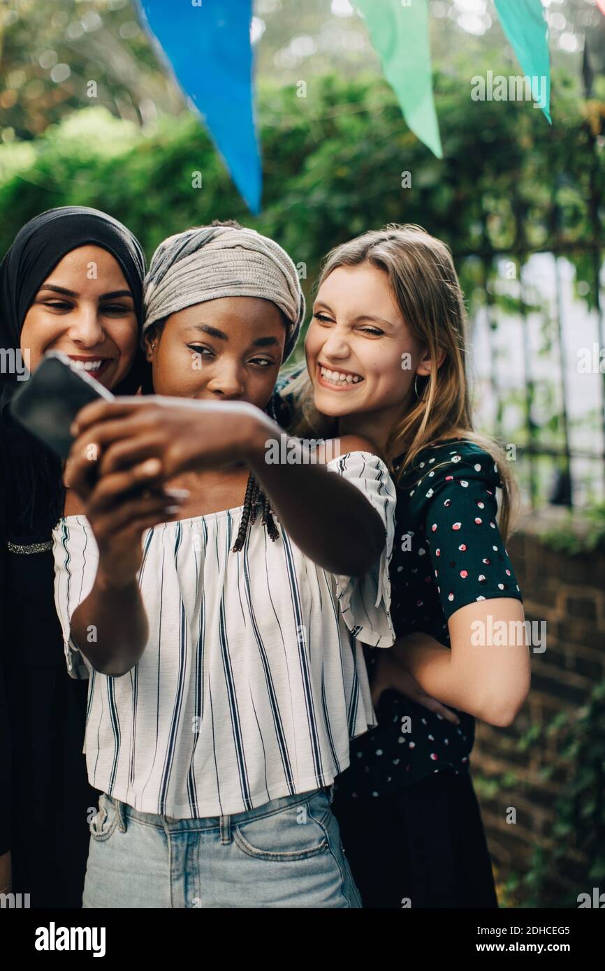 Glückliche multiethnische Freundinnen nehmen Selfie über Handy in Hinterhof Stockfoto