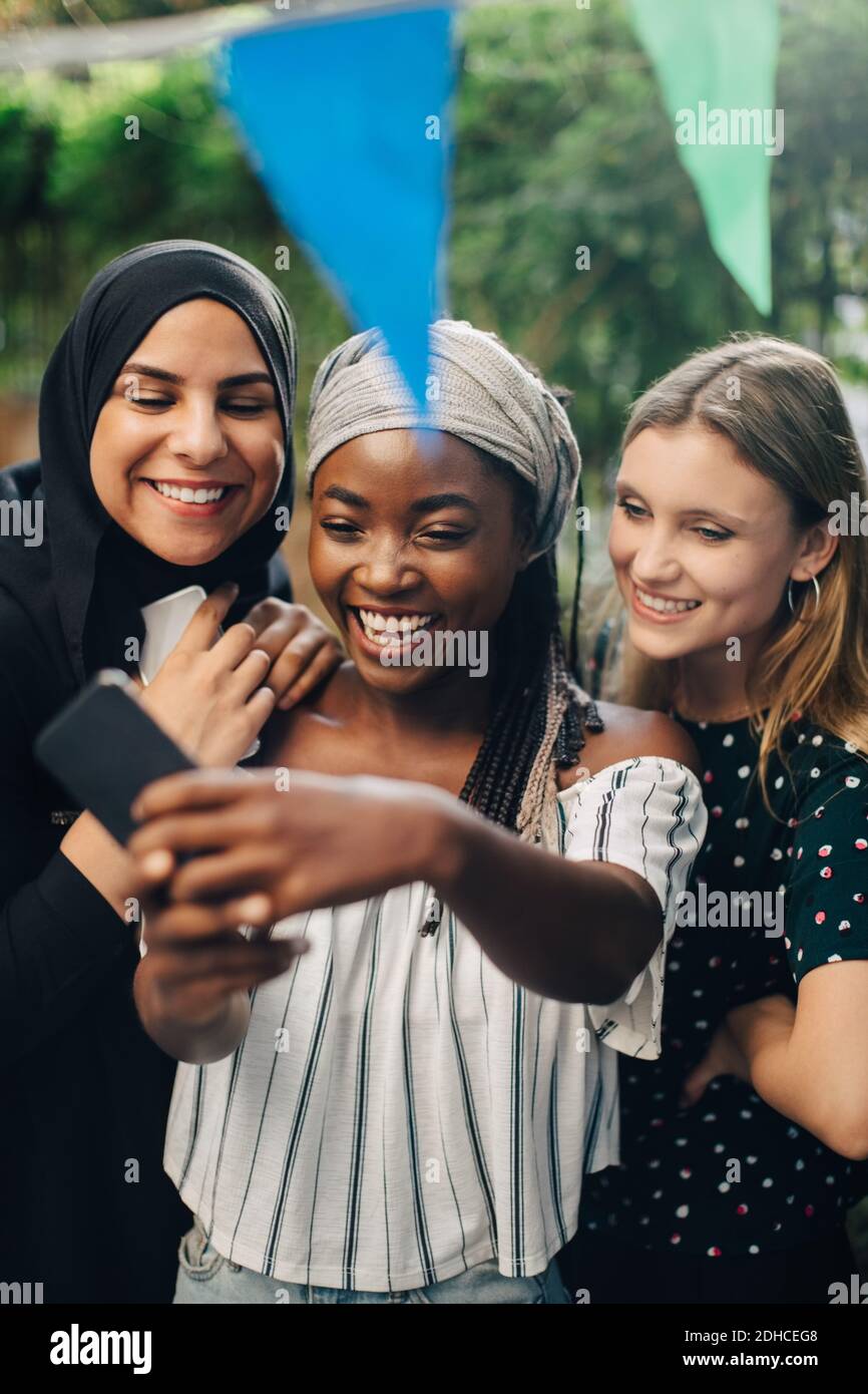 Glückliche multiethnische Freundinnen nehmen Selfie über Smartphone in Hinterhof Stockfoto