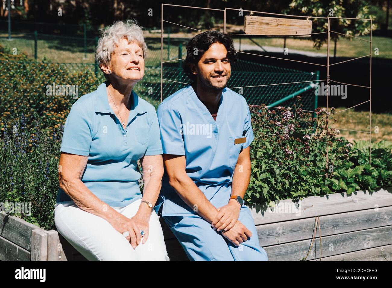 Lächelnde ältere Frau sitzt mit männlichen Krankenschwester auf Pflanzer an Hinterhof Stockfoto