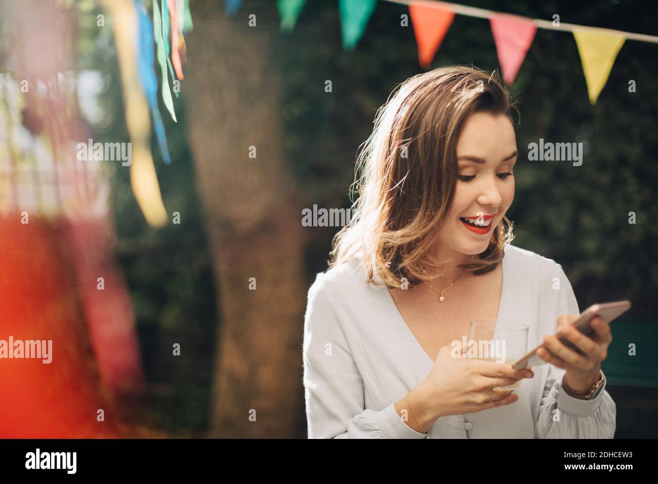 Lächelnde junge Frau mit Handy, während sie im Hinterhof steht Stockfoto
