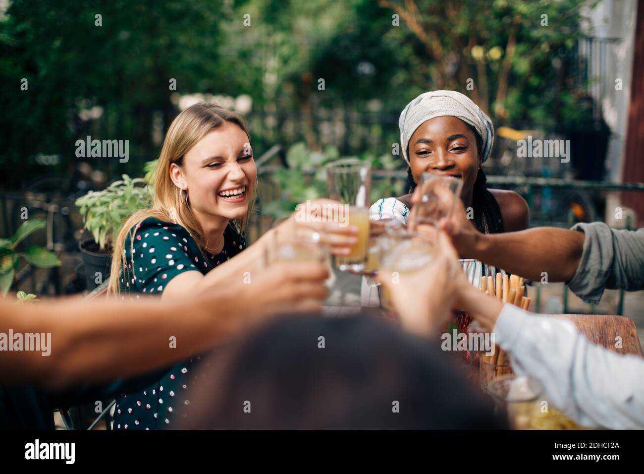 Multiethnische Freunde, die auf dem Balkon sitzen und Getränke toasten Stockfoto