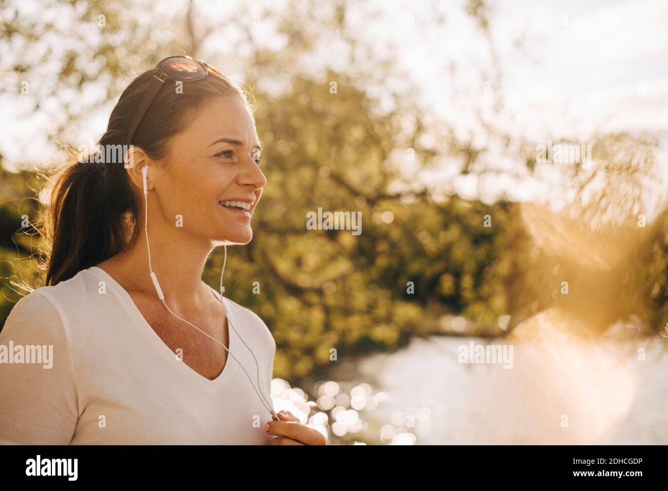 Lächelnde reife Frau im Sommerurlaub über Kopfhörer sprechen Stockfoto