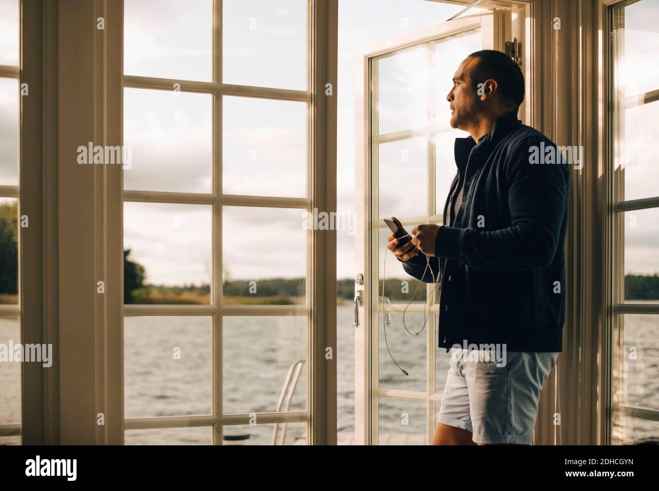 Nachdenklicher reifer Mann mit Handy, während an der Tür stehen In Ferienvilla Stockfoto