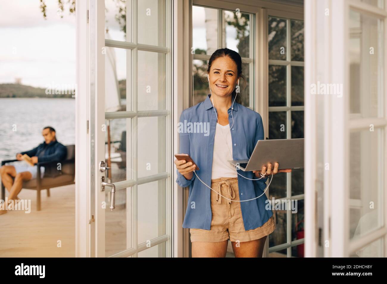 Portrait der reifen Frau mit Handy und Laptop mit Mann im Hintergrund Stockfoto