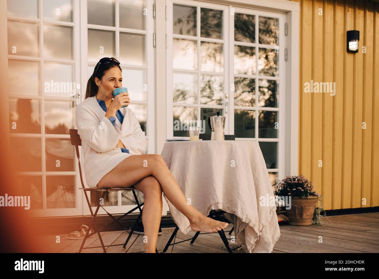 Volle Länge der reifen Frau trinken Kaffee, während sitzen an Terrasse in Ferienvilla Stockfoto