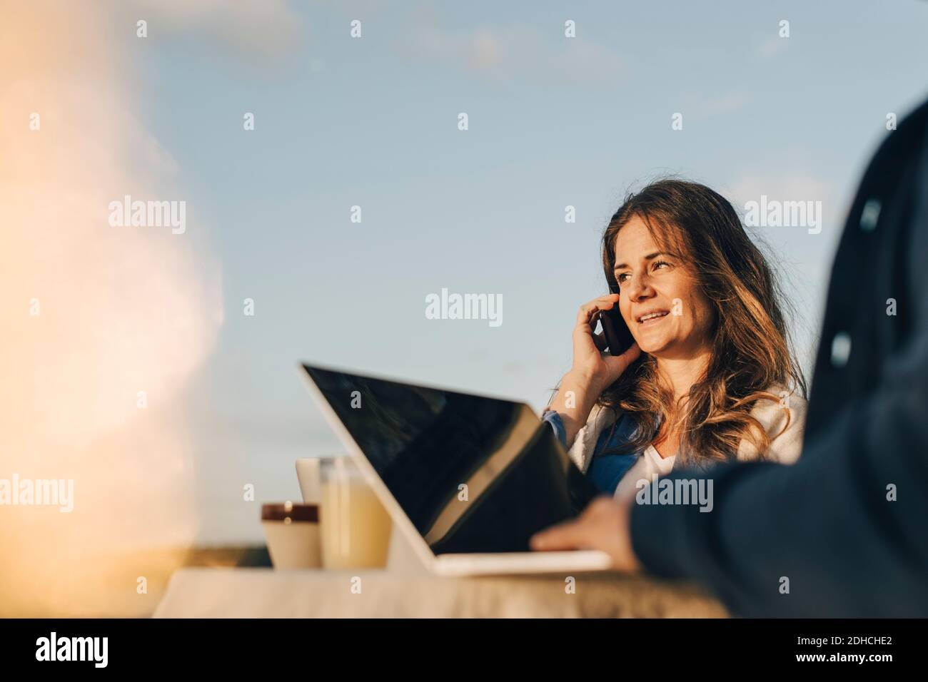 Nachdenkliche Frau mit Handy, während mit Mann gegen sitzen Himmel Stockfoto