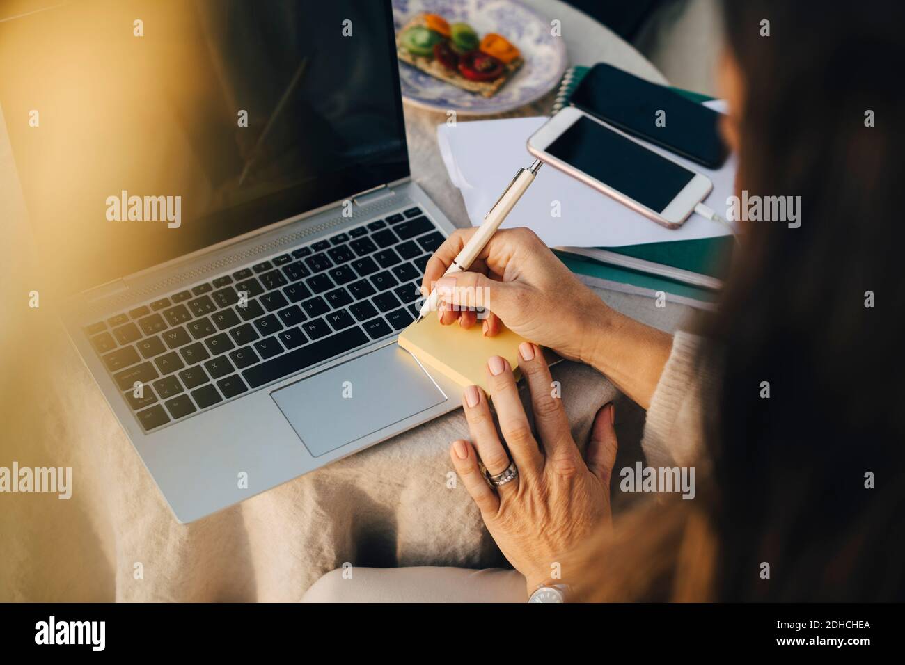 Cropped Frau schreiben auf Klebenote über Laptop am Tisch Stockfoto