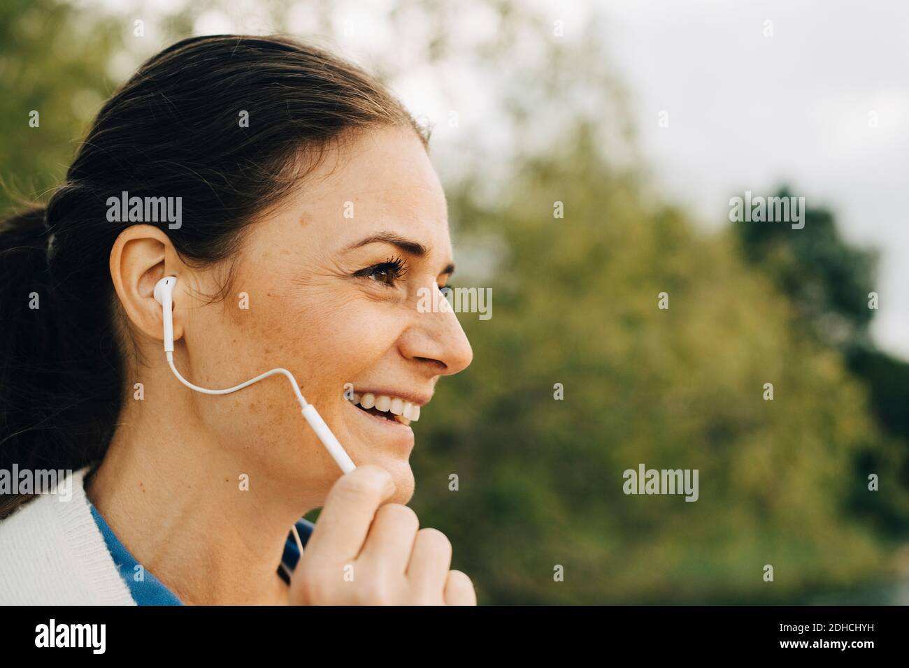 Nahaufnahme einer lächelnden Frau, die über Kopfhörer spricht, während sie wegschaut Stockfoto
