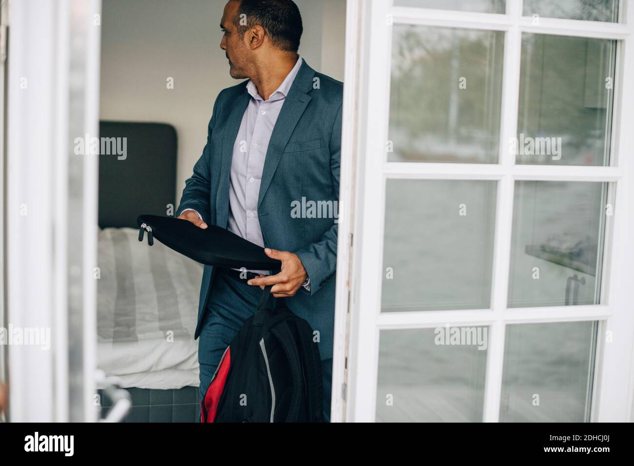 Geschäftsmann mit Laptop und Rucksack, der im Urlaub an der Tür steht villa Stockfoto