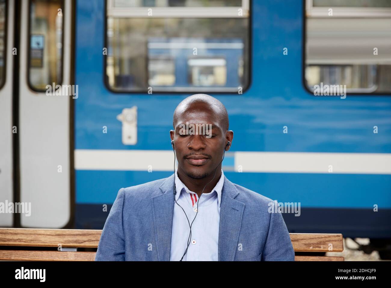 Glatze Pendler Musik hören, während sitzen mit geschlossenen Augen gegen U-Bahn am Bahnhof Stockfoto