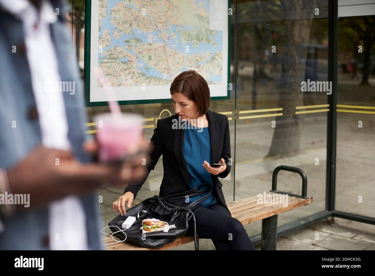 Geschäftsfrau, die Sandwich isst, während sie an der Bushaltestelle in der Stadt sitzt Stockfoto