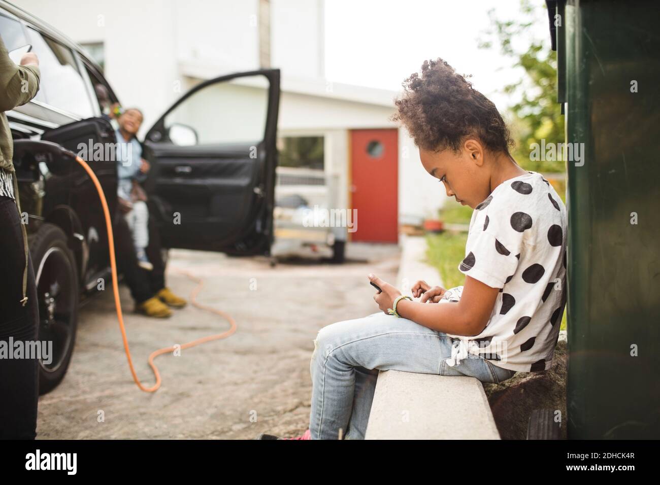 Seitenansicht des Mädchens, das Smartphone benutzt, während es innen sitzt Vorgarten Stockfoto