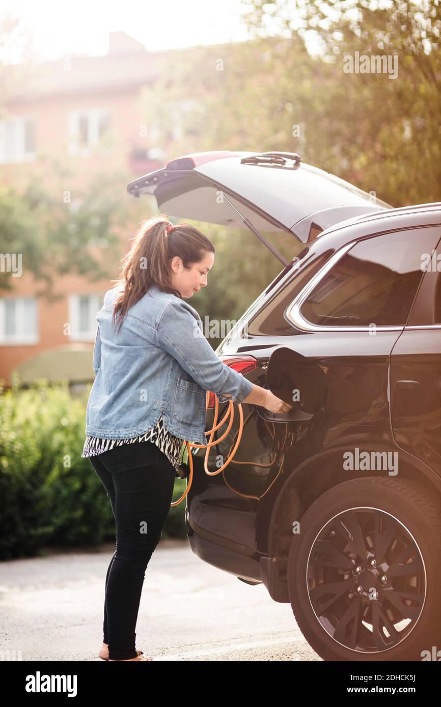 Seitenansicht der Frau, die Elektroauto auf der Auffahrt lädt Stockfoto