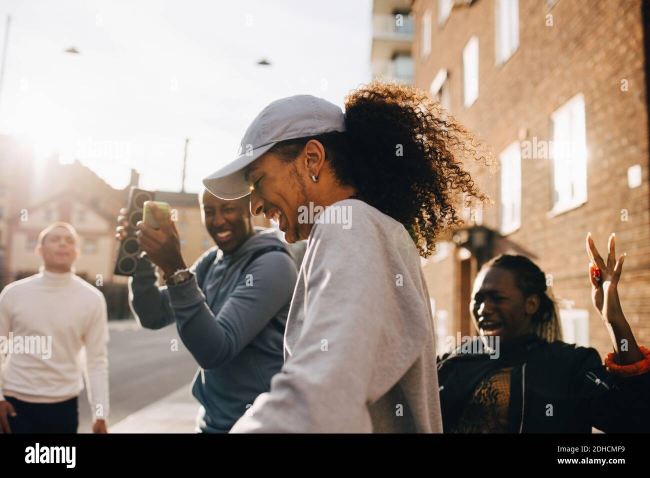 Mann mit Lautsprecher, während Freunde tanzen in der Stadt auf sonnigen Tag Stockfoto