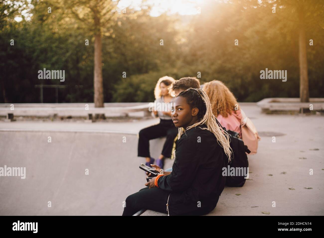 Nachdenkliche Teenager-Mädchen halten Handy, während mit Freunden sitzen Im Skateboard Park Stockfoto