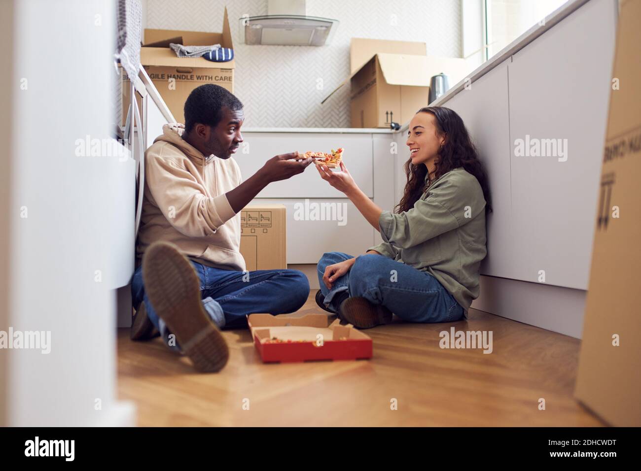 Junge gemischte Ethnizität Paar feiert bewegenden Tag in Küche Neue hausgemachte Pizza zum Mitnehmen auf dem Boden, umgeben von Entnahmeboxen zusammen Stockfoto