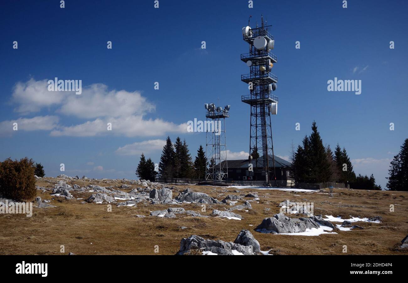 Kommunikationsturm mit Mikrowellenrelais-Geschirr auf dem Schoeckl in Österreich im Spätswinter. Es gibt Flecken von Schnee auf dem Gras um ihn herum. Stockfoto