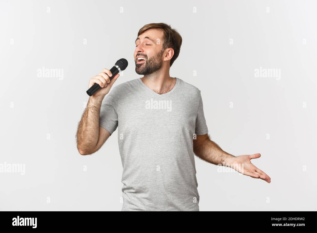 Schöner sorgloser Kerl, der Lied in Karaoke singt, Mikrofon hält und auf weißem Hintergrund steht Stockfoto