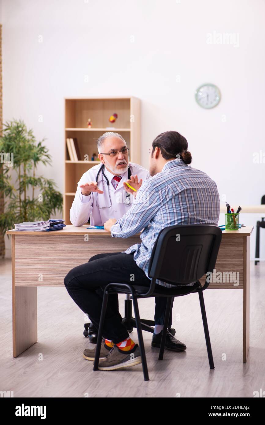 Junger männlicher Patient besucht alten männlichen Arzt Stockfoto