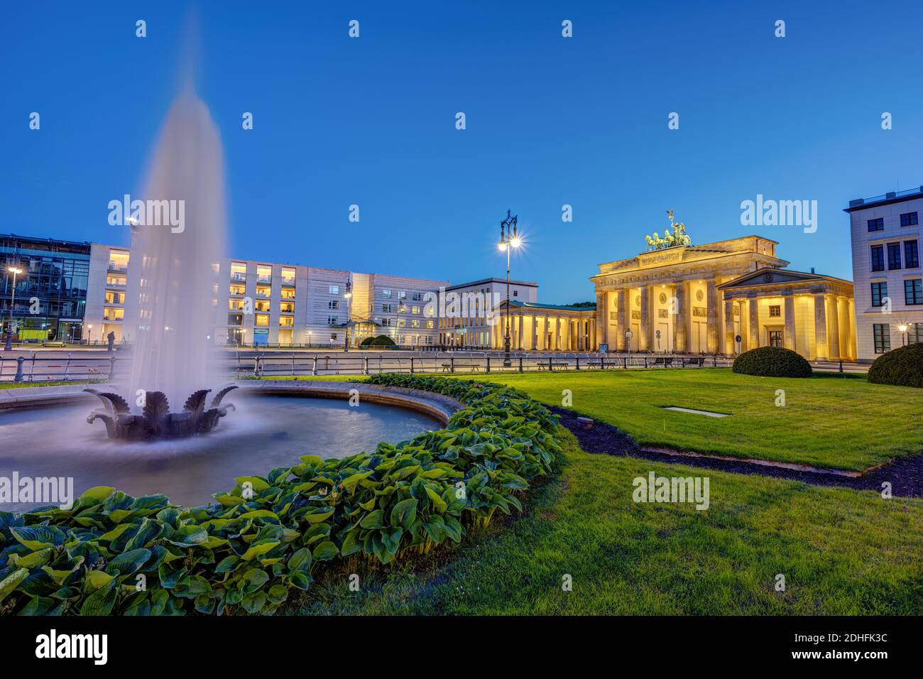 Das beleuchtete Brandenburger Tor in Berlin bei Dämmerung mit einem Brunnen Stockfoto