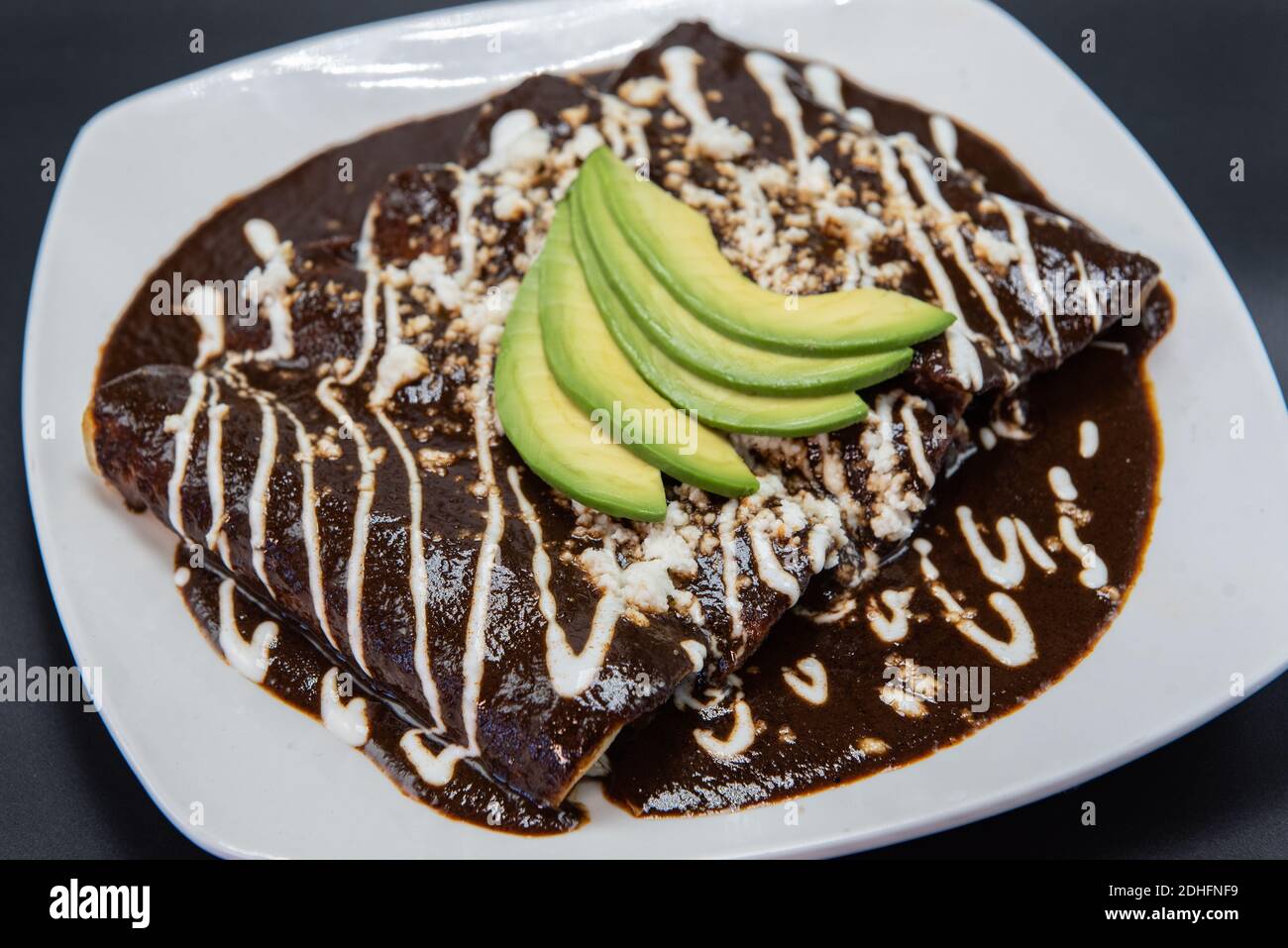 Huhn Enchiladas erstickt in Käse und rote Sauce perfekt auf dem Grill mit Bohnen und Avocado auf der Oberseite vorbereitet. Stockfoto