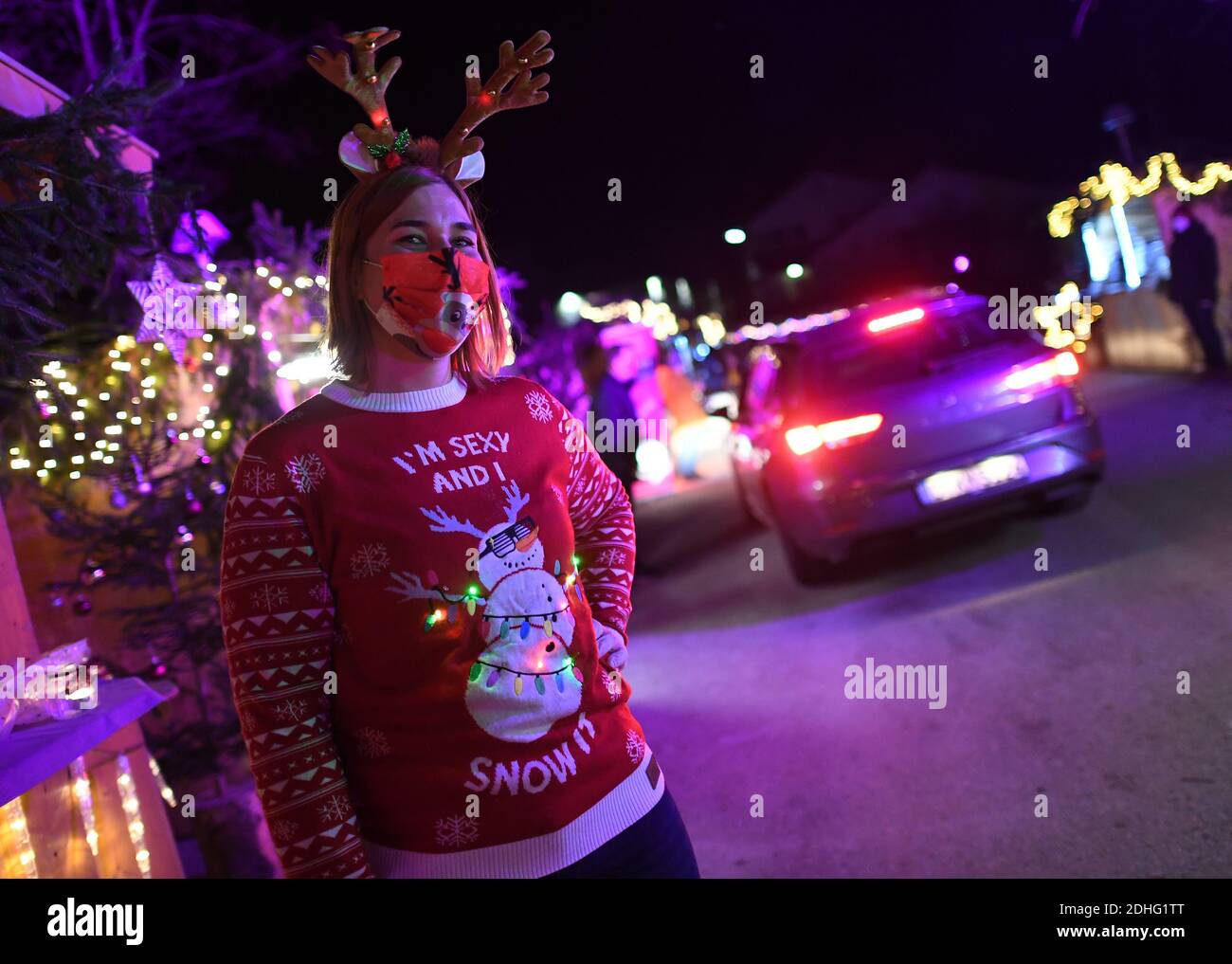 Murnau, Deutschland. Dezember 2020. Ein Mitarbeiter in einem Weihnachtspullover steht auf dem Drive-in-Weihnachtsmarkt. Man darf nicht aus dem Auto aussteigen und der Verkehr ist nur eine Richtung, aber man bekommt alle Arten von Leckereien im Fahrzeug von den Weihnachtsbuden serviert. Quelle: Angelika Warmuth/dpa/Alamy Live News Stockfoto