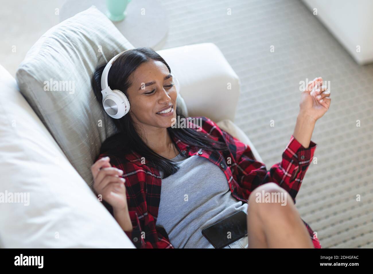 Mixed-Race-Frau auf der Couch liegend mit Kopfhörern hören Musik zu Hause Stockfoto