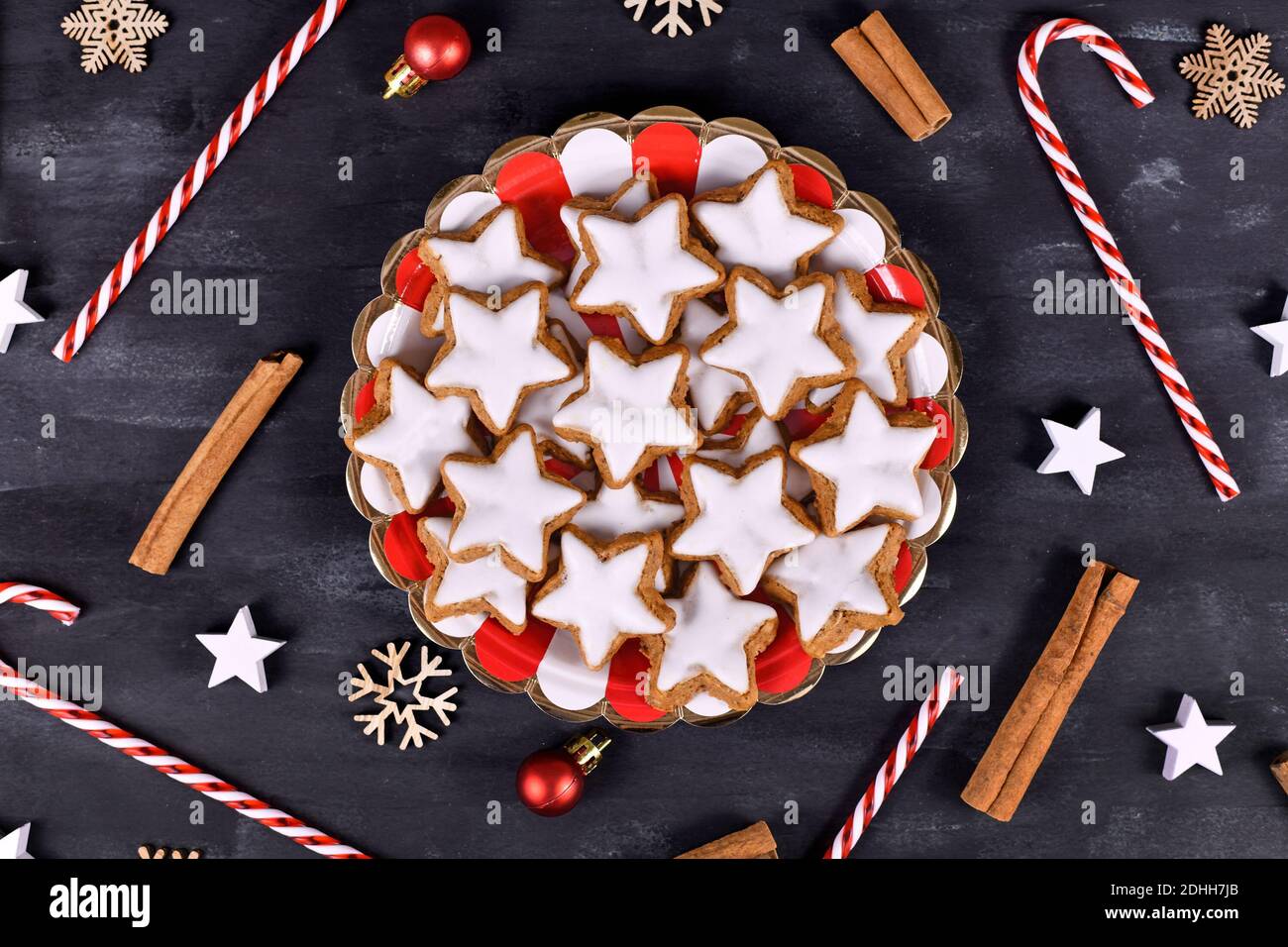Deutsche sternförmige glasierte Zimt Weihnachtsplätzchen genannt 'Zimtsterne' auf Gestreifter Teller, umgeben von Zimtstangen und saisonaler Dekoration Stockfoto