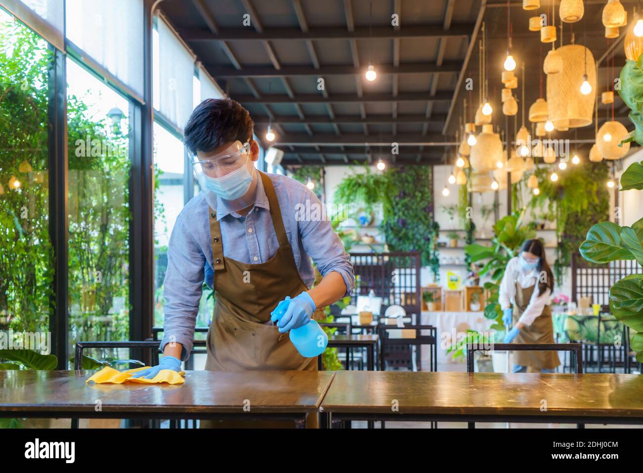 Portrait Attraktive asiatische Restaurant Mitarbeiter tragen Gesichtsmaske und Gesicht Reinigungstisch und Boden mit Alkohol und nassem Tuch abschirmen Vor der Begrüßung custome Stockfoto