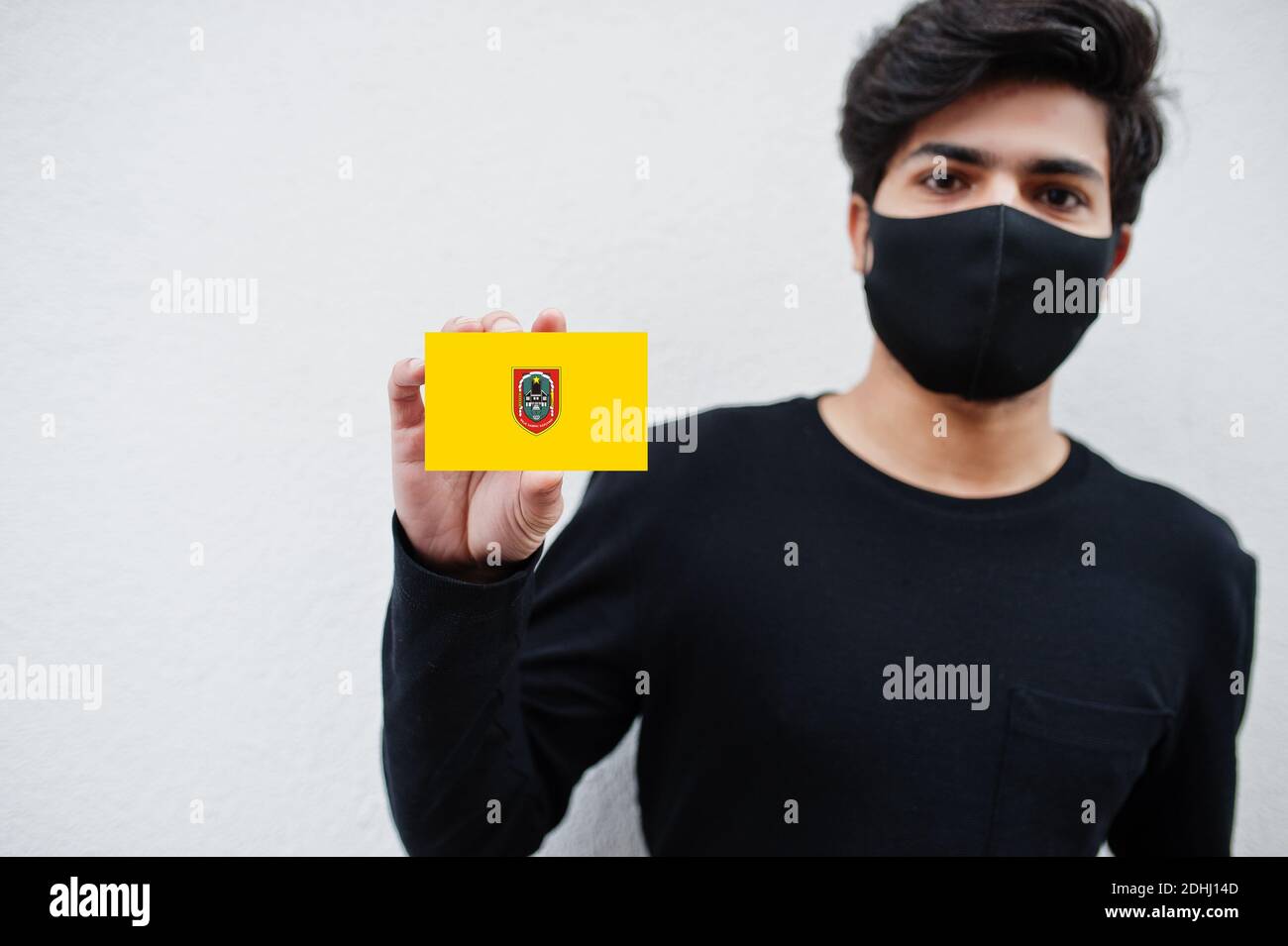 Indonesian Mann tragen ganz schwarz mit Gesichtsmaske halten Süd Kalimantan Flagge in der Hand isoliert auf weißem Hintergrund. Provinzen von Indonesien Coronavirus conce Stockfoto