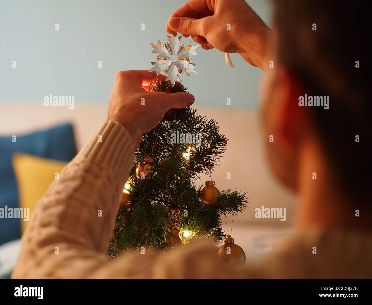 Kaukasischer junger Mann neben einem Weihnachtsbaum in einem Wollpullover, der ein Geschenk in den Händen hält. Er genießt die Ferien in einem gemütlichen Zuhause. Stockfoto