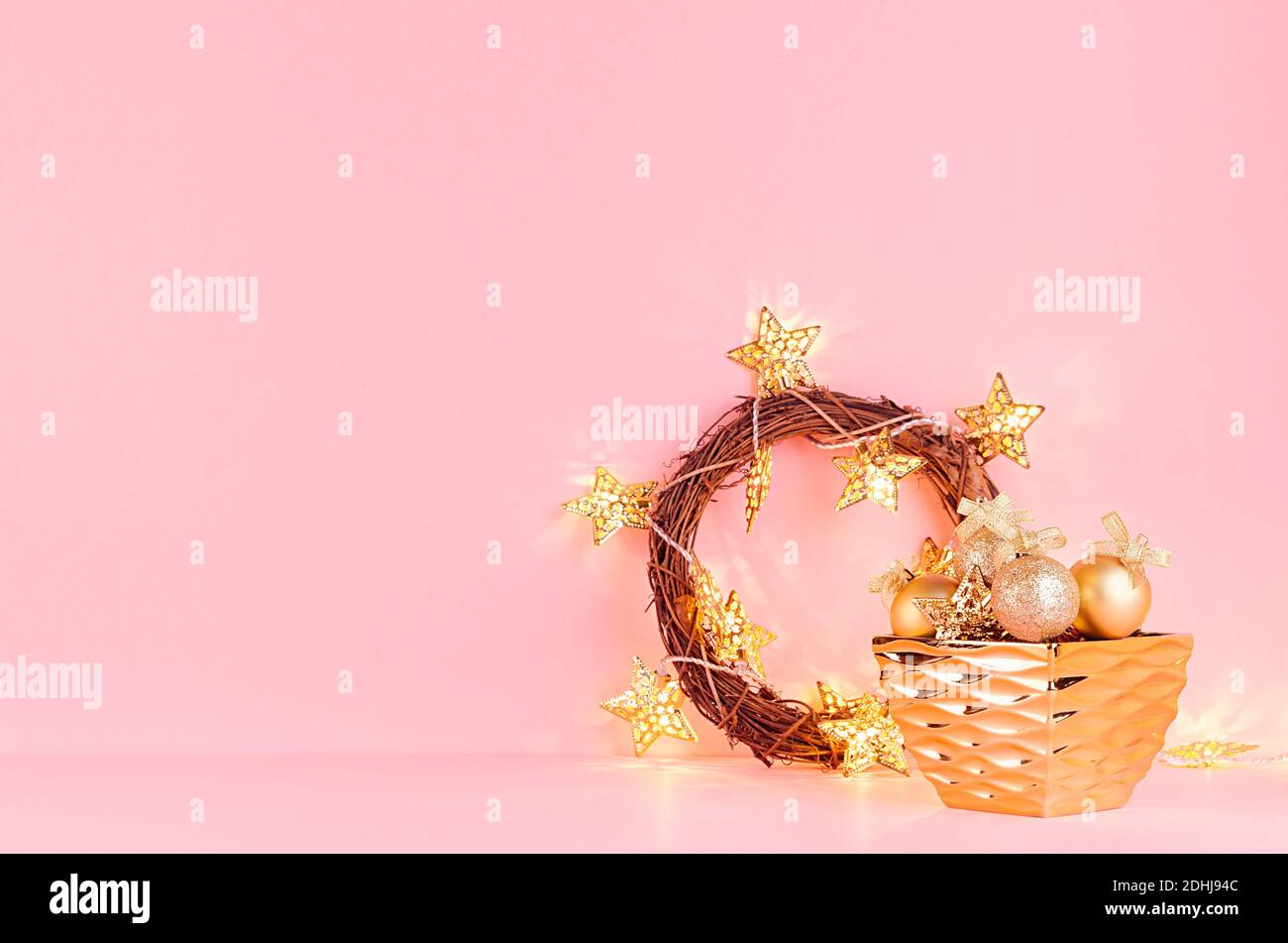 Gold weihnachtskranz mit leuchtenden Sternen Lichter, Kugeln, Geschenk auf eleganten pastellrosa Hintergrund. Stockfoto