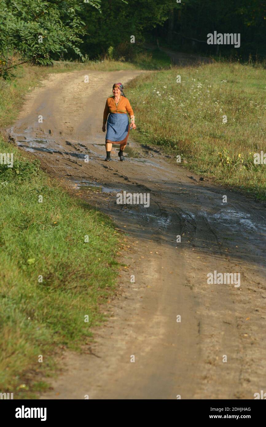 Old County, Rumänien. Ältere Frau, die auf einer unbefestigten Straße außerhalb des Dorfes geht. Stockfoto
