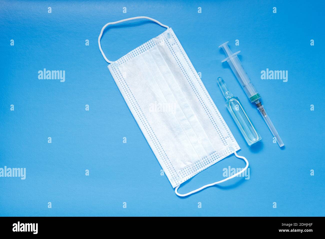 Eine Ampulle mit einem Impfstoff, eine medizinische Maske und eine Spritze liegen auf blauem Hintergrund. Das Konzept der Impfung gegen Coronavirus. Speicherplatz kopieren. Stockfoto