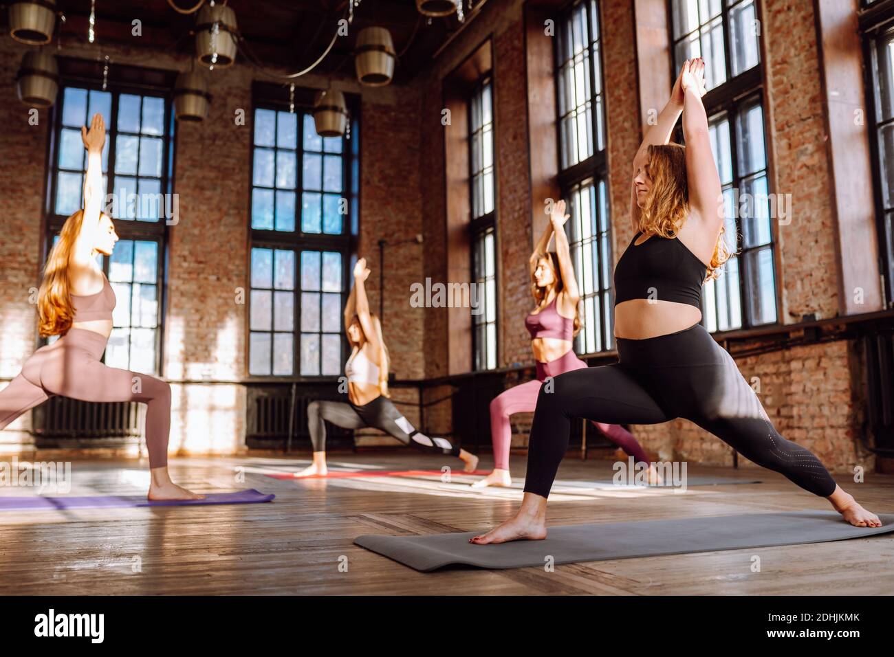 Gruppe von vier Frauen machen Yoga-Praxis in großen Loft-Klasse stehen in Warrrior Pose. Entspannung, Meditation. Virabhadrasana Stockfoto