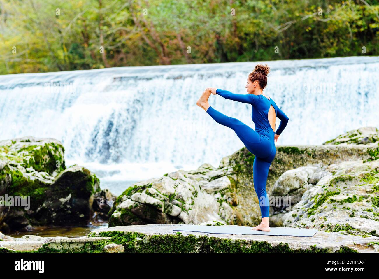 Seitenansicht des weiblichen Balancierens auf Matte in Hasta Padangusthasana Und Achtsamkeit in der Nähe von Wasserfall in der Natur üben Stockfoto