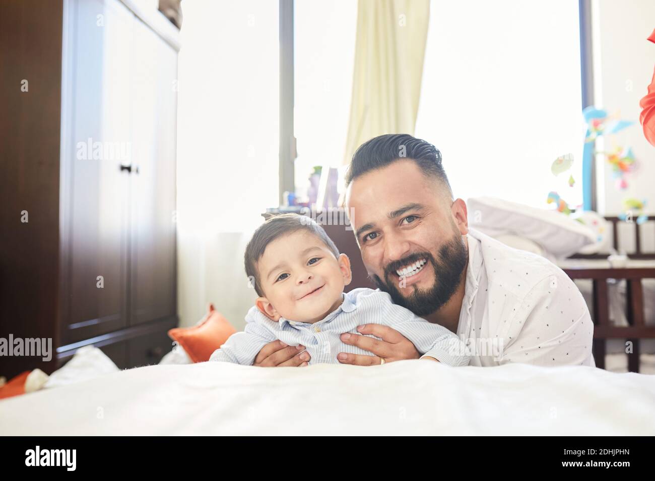 Begeistert hispanischen Vater mit Spaß mit liebenswert kleinen Kind während Verbringen Sie Zeit zusammen zu Hause mit Blick auf die Kamera Stockfoto