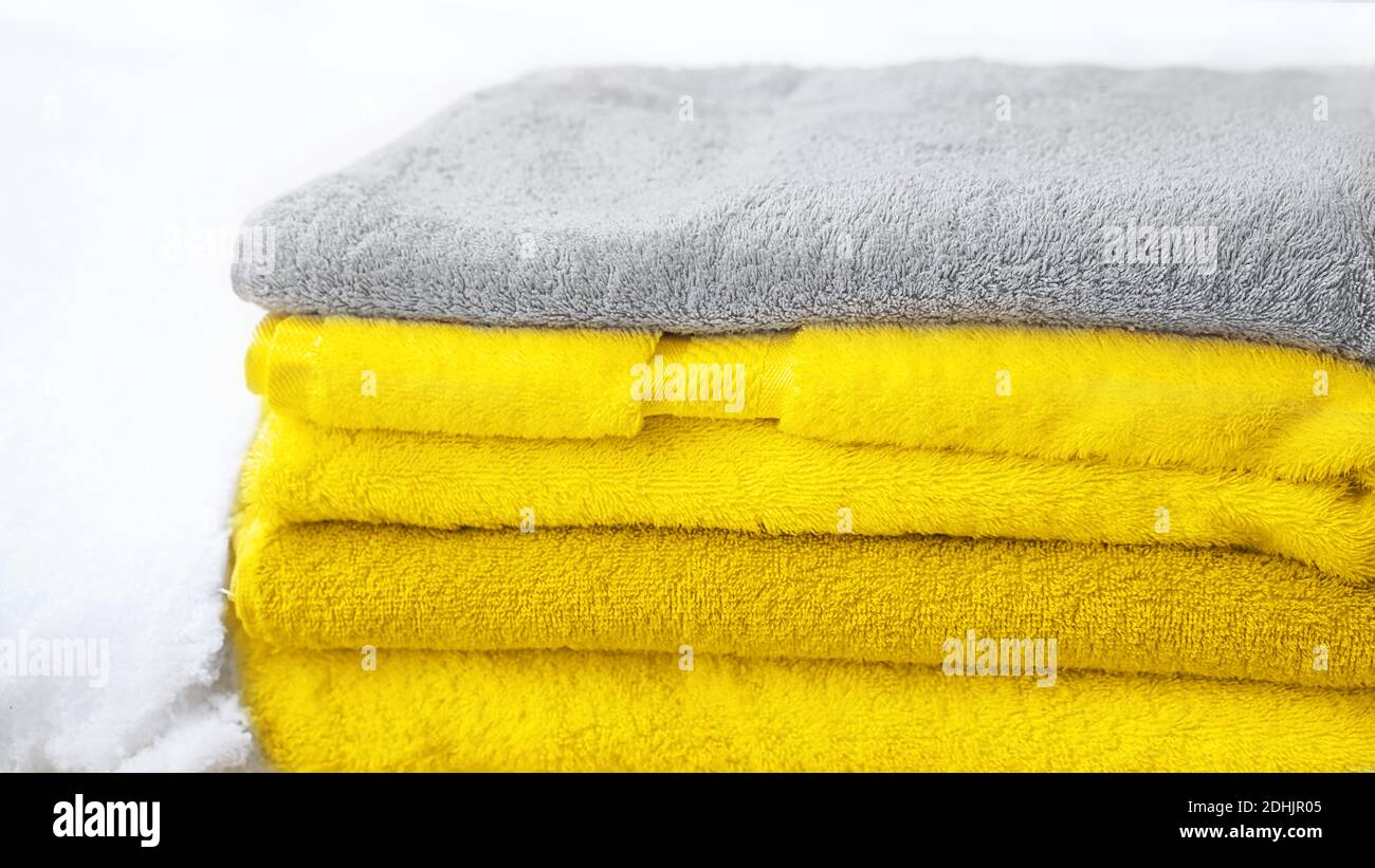 Stapel von Handtüchern in Farbe des Jahres 2021 - hell leuchtende gelbe und graue Farben auf weißem Schnee, isoliert. Konzept der Farbe des Jahres 2021. Stockfoto