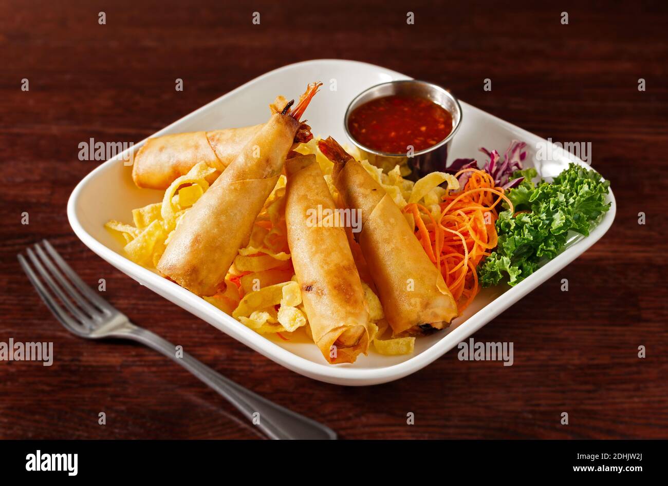 Thai gebratene Garnelenrollen mit Chilisauce und Gemüse in Ein weißer Teller auf einem dunklen Holztisch Stockfoto