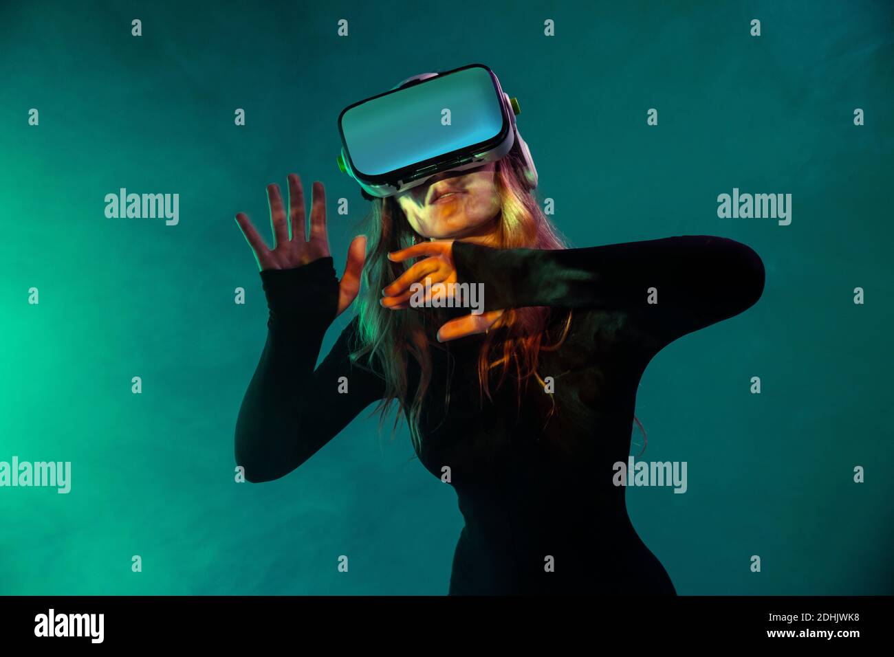 Junge unerkennbare blonde Frau, die Luft berührt und Virtual Reality-Headset auf buntem blauem Neon-Beleuchtung Studio-Hintergrund trägt Stockfoto