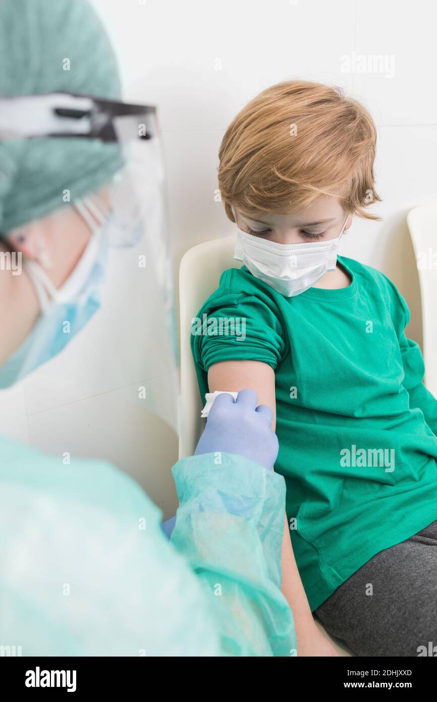 Seitenansicht des Sanitäter in Schutzkostüm desinfizierende Haut von Patient mit Alkohol vor der Injektion Stockfoto