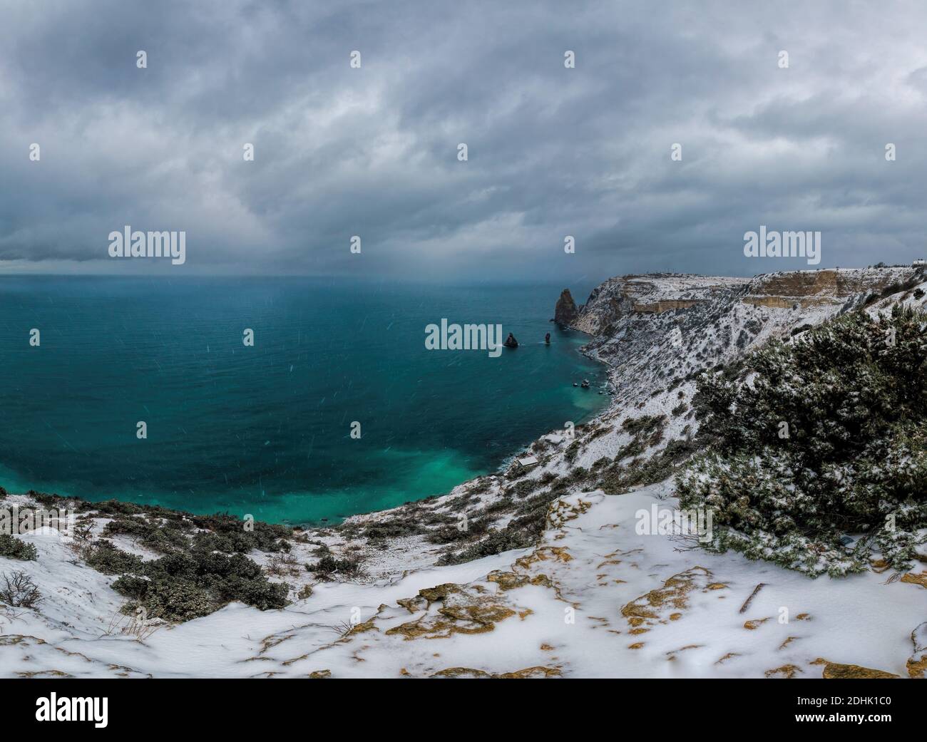 Schneebedeckte Felsklippen über dem Meer. Winter Sonnenuntergang über der Meeresbucht. Wacholderbaum unter Schnee. Konzept von Winterurlaub, Reisen, Abenteuer und Stockfoto