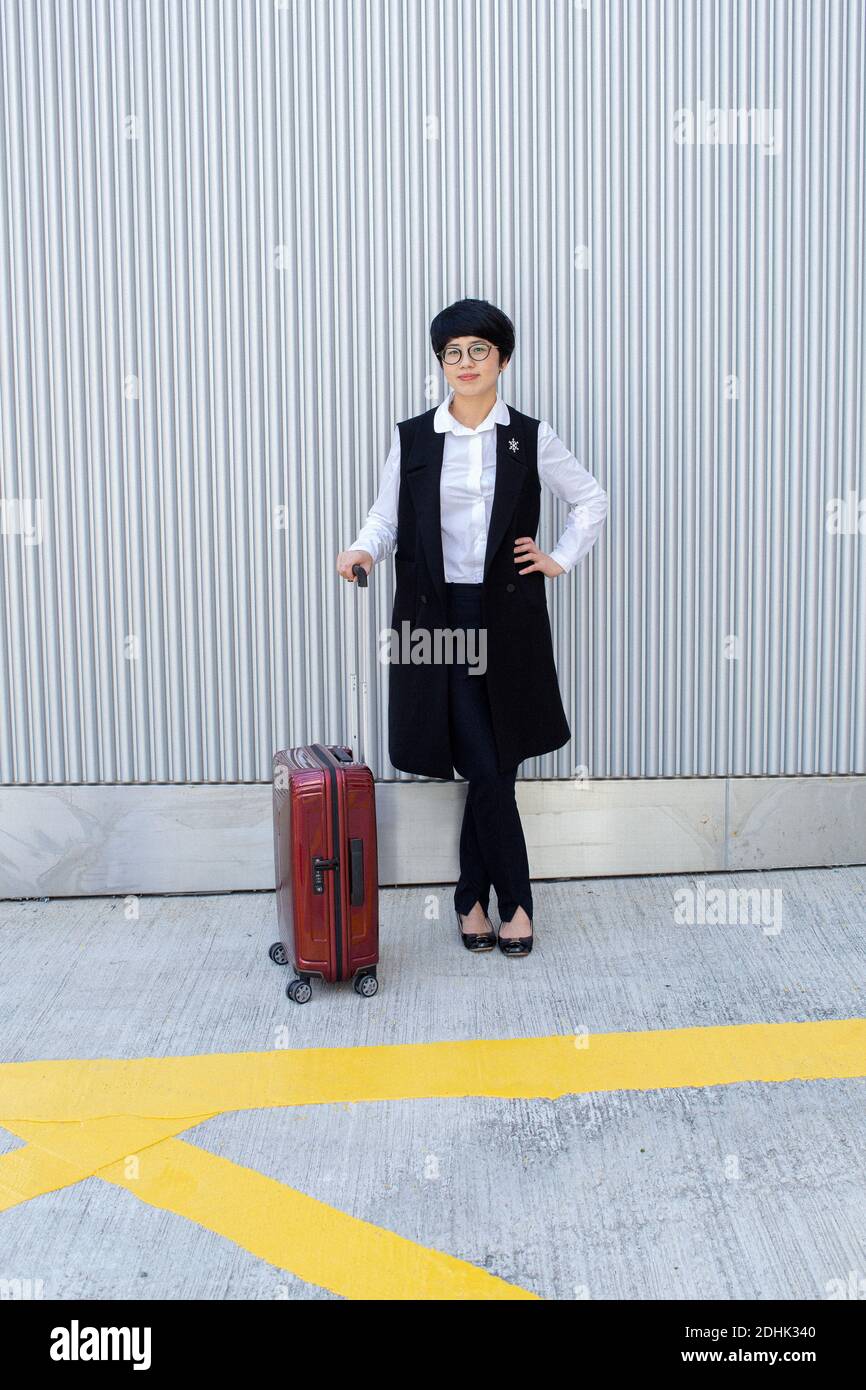 Asiatische Geschäftsfrau, die mit Gepäck im Freien steht. Asiatische Frau, die in Hongkong steht und Gepäck hält. Stockfoto