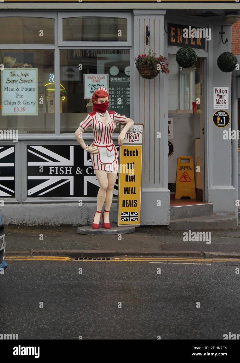 Weibliche Schaufensterpuppe in rot und weiß Kellnerin Uniform gekleidet tragen Ein Schal als Gesichtsmask außerhalb eines Chipshops Stockfoto