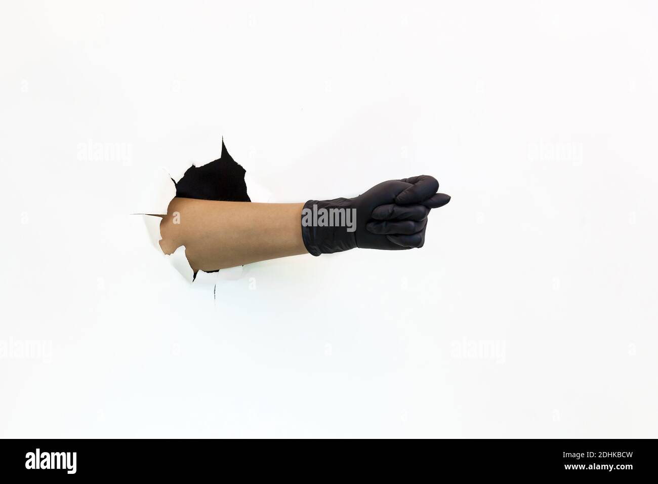 Weibliche Hand in schwarzem Latex-Handschuh durch zerrissenes Papier auf weißem Hintergrund zeigt Geste Abb. Quarantänemaßnahmen zur Verhinderung der Ausbreitung von Covid 19. Ha Stockfoto