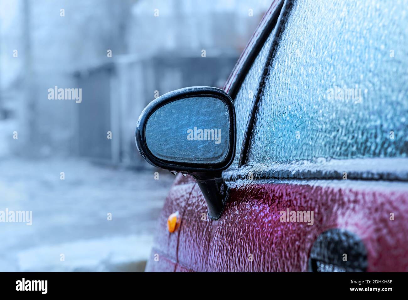 Der Außenspiegel des Autos fror nach dem Glatteisregen. Abnormes Wetter, eisiger Regen bedeckte das rote Auto mit Eiskruste. Soft-Focus-Technik Stockfoto
