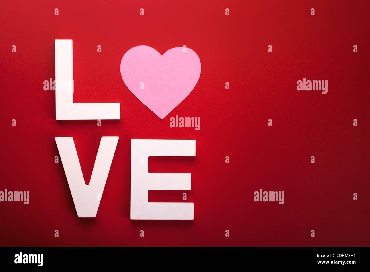 Alles Liebe zum Valentinstag. Das Wort Liebe in weißem Holz mit einem rosa Herz auf rotem Hintergrund Stockfoto