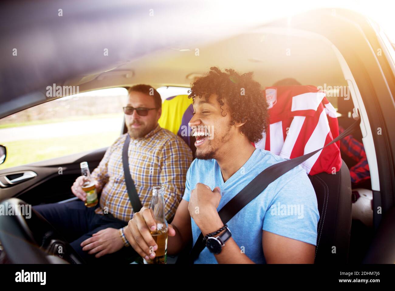 Porträt eines betrunkenen jungen Afro-amerikaners, der mit einem Bier in den Händen lacht und fährt, während seine Freunde Spaß im Auto haben. Stockfoto