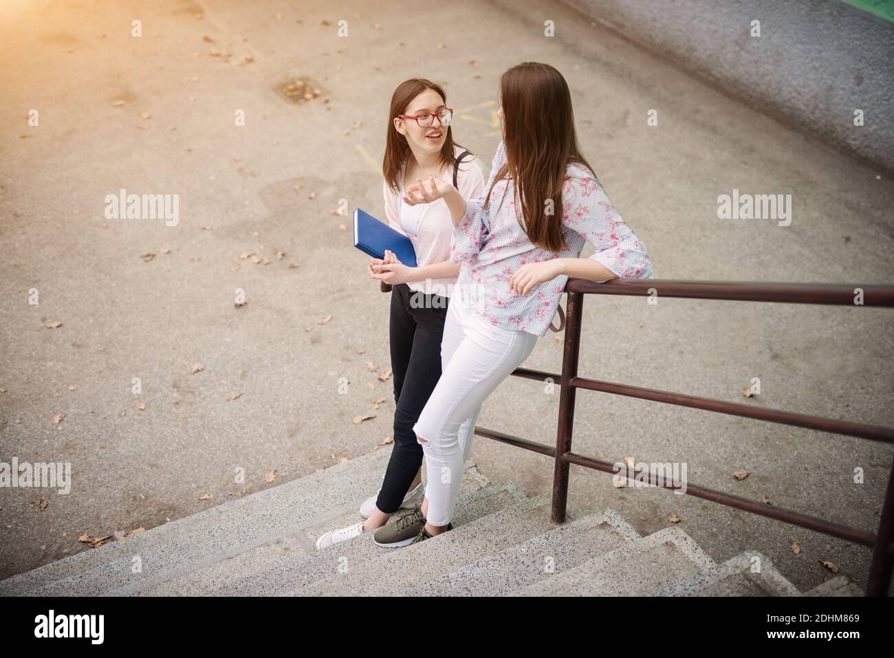 Zwei charmante High School Mädchen stehen auf Treppen gegen den Zaun lehnen und eine Unterhaltung. Stockfoto